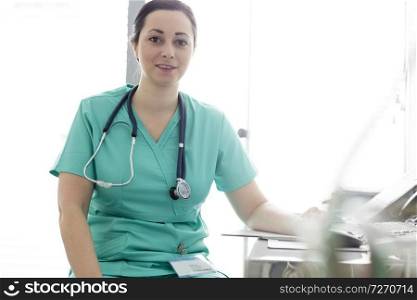 Portrait of confident smiling nurse with stethoscope at desk in hospital