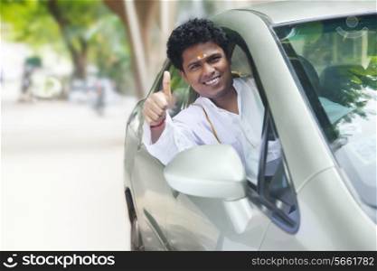Portrait of confident South Indian man gesturing thumbs up in new car