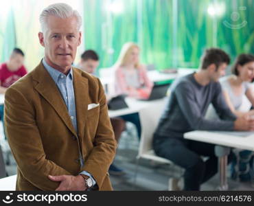 portrait of confident teacher in school classroom, students group on class in background