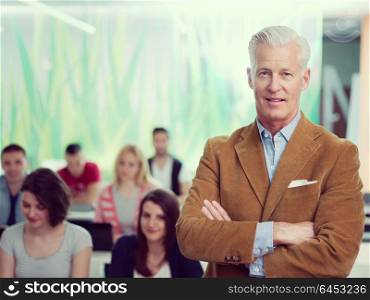 portrait of confident teacher in school classroom, students group on class in background
