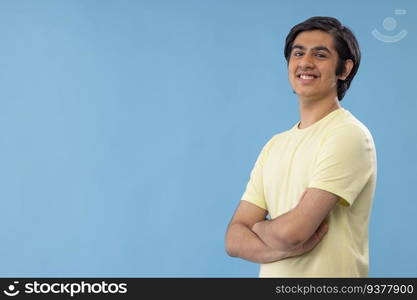 Portrait of confident teenage boy with hands folded standing against blue background