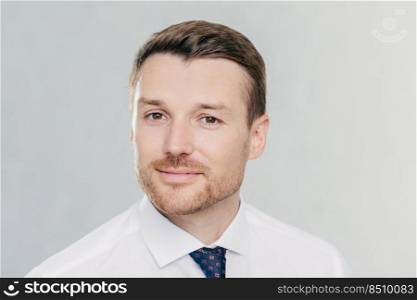 Portrait of confident unshaven businessman looks with self assured expression, ready to sign contract, poses in office against white background, wears white shirt and elegant tie. Business and people