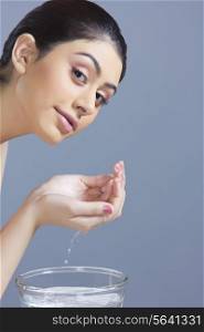 Portrait of confident woman washing face with water against blue background