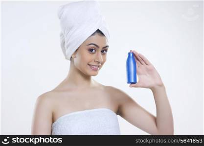 Portrait of confident woman wrapped in towel holding hair oil bottle against gray background