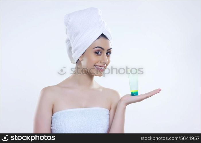 Portrait of confident woman wrapped in towel showing beauty product over white background