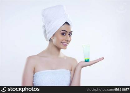 Portrait of confident woman wrapped in towel showing beauty product over white background