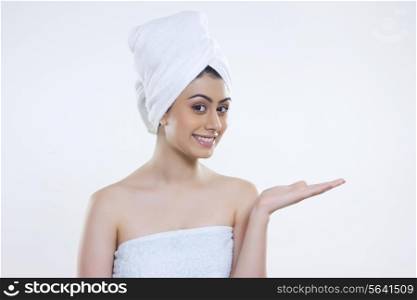 Portrait of confident woman wrapped in towel showing invisible product over white background
