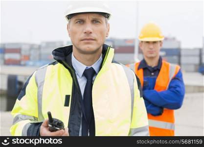 Portrait of confident worker standing with coworker in background at shipping yard