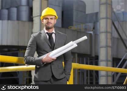 Portrait of confident young architect holding blueprints outside industry