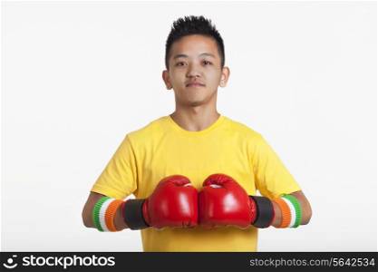 Portrait of confident young boy wearing red boxing gloves over white background