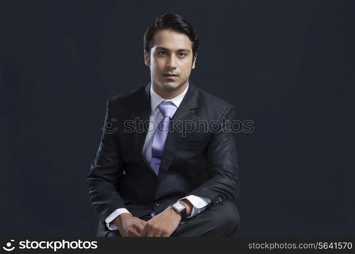 Portrait of confident young businessman against black background