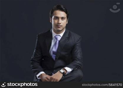 Portrait of confident young businessman against black background