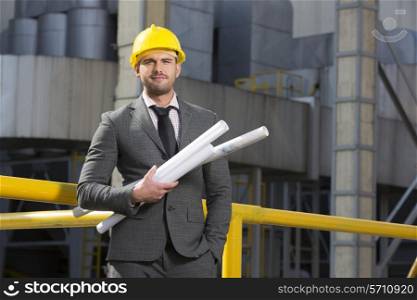 Portrait of confident young businessman holding blueprints outside industry