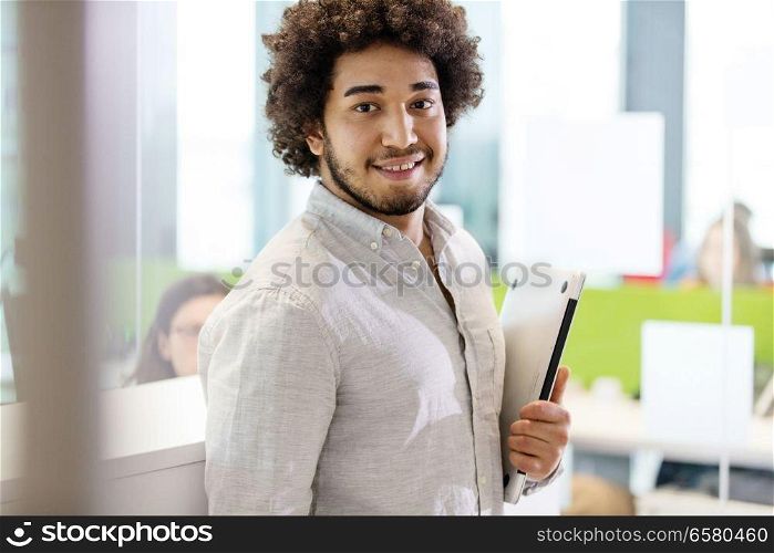 Portrait of confident young businessman holding laptop in office