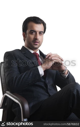 Portrait of confident young businessman sitting on chair against white background