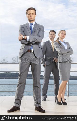 Portrait of confident young businessman standing with coworkers on terrace against sky