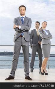 Portrait of confident young businessman standing with coworkers on terrace against sky
