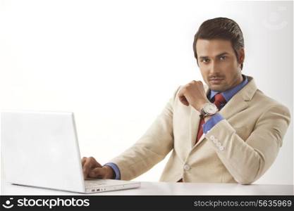 Portrait of confident young businessman using laptop at office desk