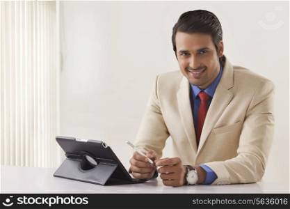 Portrait of confident young businessman with digital tablet at office desk