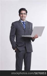 Portrait of confident young businessman with laptop against gray background