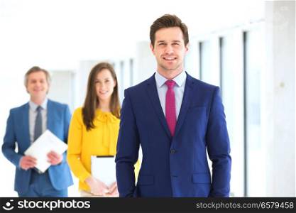 Portrait of confident young businessman with team in background at office