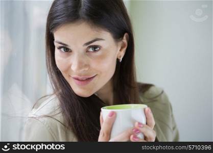 Portrait of confident young businesswoman with coffee cup in office