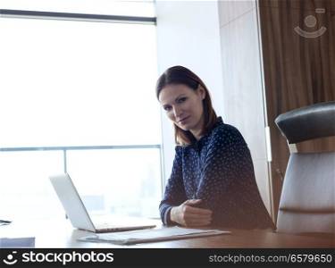 Portrait of confident young businesswoman with laptop at desk in office