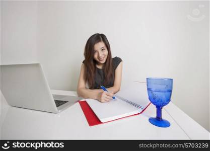 Portrait of confident young businesswoman writing on diary at office desk