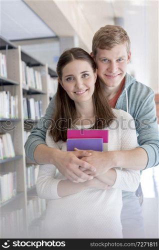 Portrait of confident young couple embracing at library in university