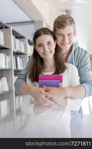 Portrait of confident young couple embracing at library in university