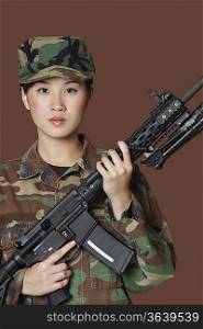 Portrait of confident young female Marine Corps soldier holding M4 assault rifle over brown background