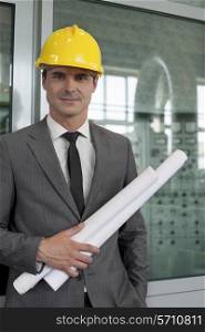 Portrait of confident young male architect holding blueprints in industry