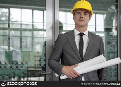 Portrait of confident young male architect holding rolled up blueprints in industry