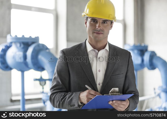 Portrait of confident young male supervisor writing on clipboard in industry