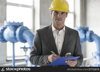Portrait of confident young male supervisor writing on clipboard in industry