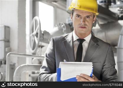 Portrait of confident young male supervisor writing on clipboard in industry