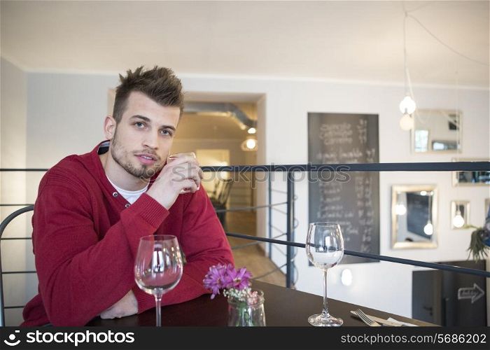 Portrait of confident young man drinking water from glass in cafe