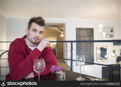 Portrait of confident young man drinking water from glass in cafe