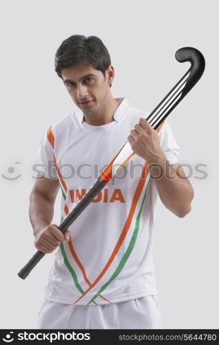 Portrait of confident young man holding hockey stick isolated over gray background