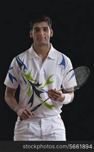 Portrait of confident young man with badminton racket over black background