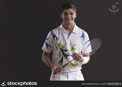 Portrait of confident young man with tennis racket standing against black background