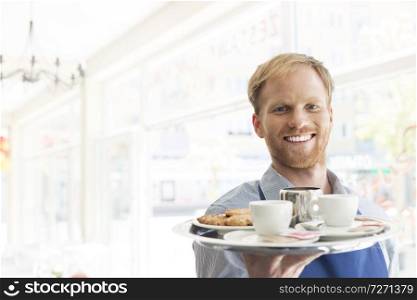Portrait of confident young waiter serving espresso coffee at restaurant