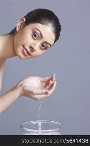 Portrait of confident young woman washing face with water against blue background