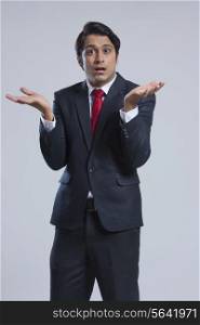 Portrait of confused businessman gesturing against gray background