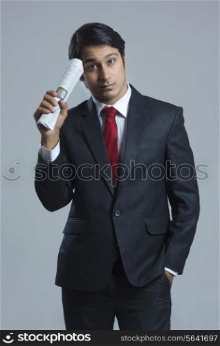 Portrait of confused businessman holding newspaper over gray background