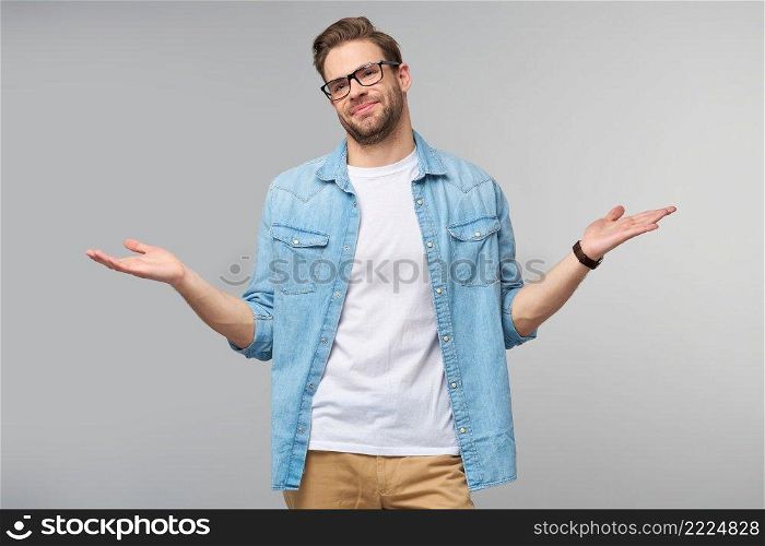 Portrait of confused clueless young man in jeans shirt standing over grey background.. Portrait of confused clueless young man in jeans shirt standing over grey background