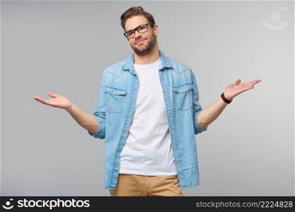 Portrait of confused clueless young man in jeans shirt standing over grey background.. Portrait of confused clueless young man in jeans shirt standing over grey background