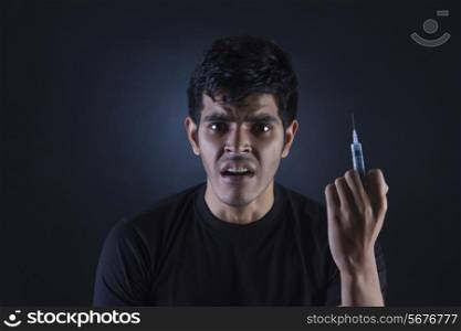 Portrait of confused drug addict with syringe against black background
