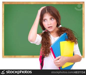 Portrait of confused school girl holding head by hand on green chalkboard background, didn't know answer on question, difficult test concept