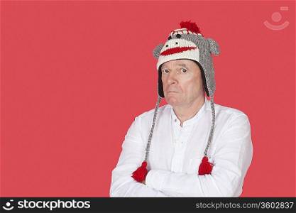 Portrait of confused senior man with arms crossed against red background